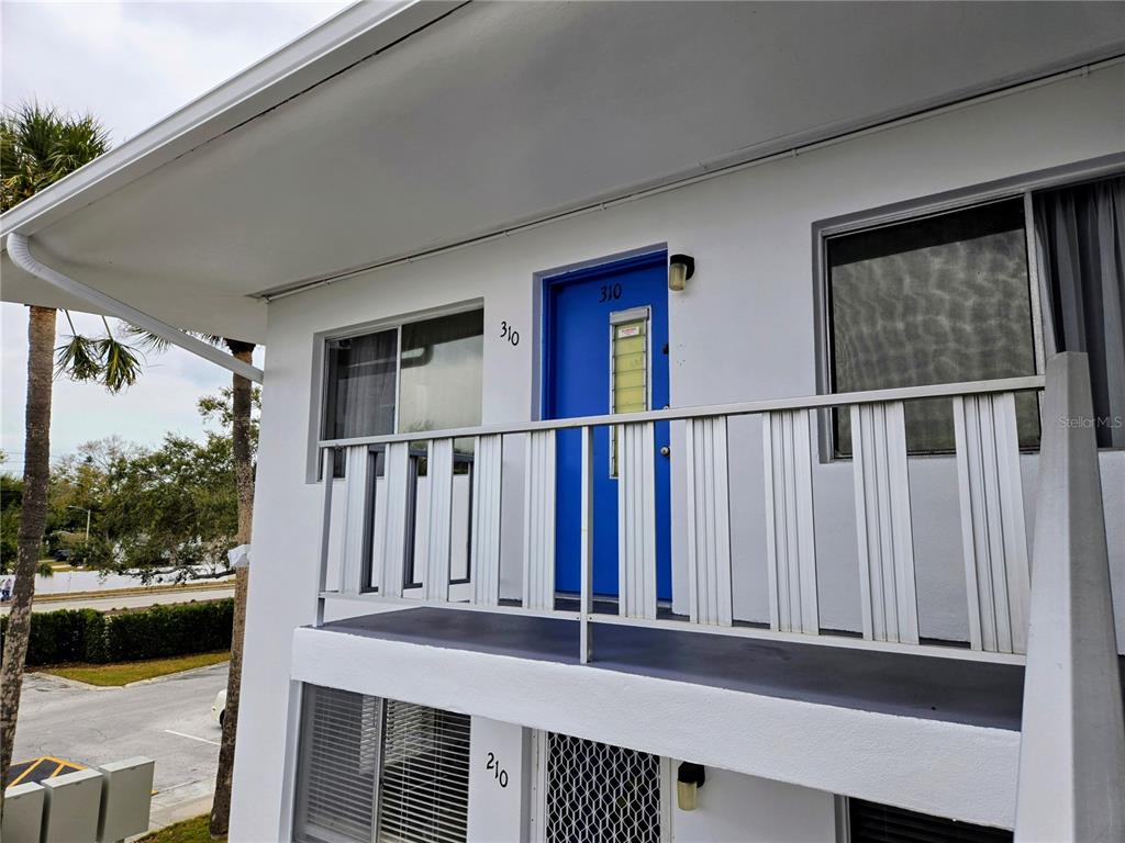 An exterior view of a white building showing a blue door labeled 310 and a balcony — 11251 80TH AVENUE UNIT 310, SEMINOLE, FL