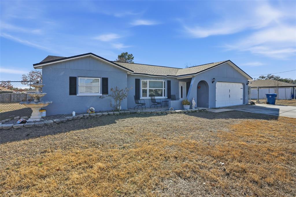 A single-story blue house with a white garage door, a front patio, and a fountain — 13380 BARLINGTON STREET, SPRING HILL, FL