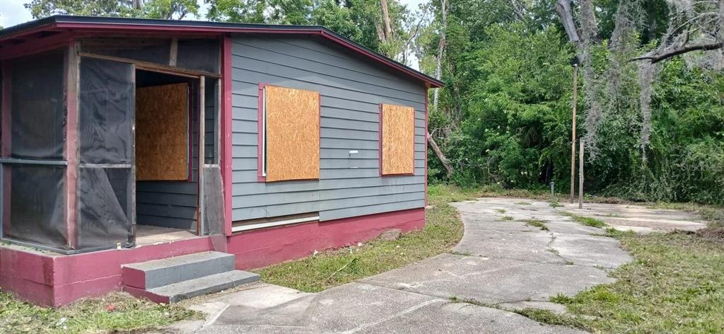 A small, gray-sided house with boarded-up windows and a screened porch sits on a lot — 5851 DUNMIRE AVENUE, JACKSONVILLE, FL