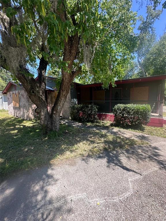 A single-story house with a stone facade, boarded-up windows, and a large tree in front — 5851 DUNMIRE AVENUE, JACKSONVILLE, FL