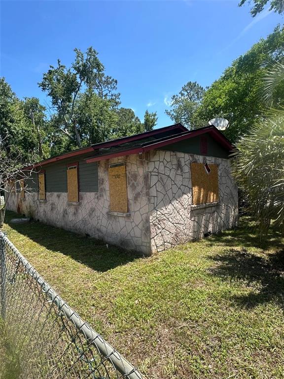 A single-story house with stone veneer siding and boarded-up windows sits on a grassy lot — 5851 DUNMIRE AVENUE, JACKSONVILLE, FL