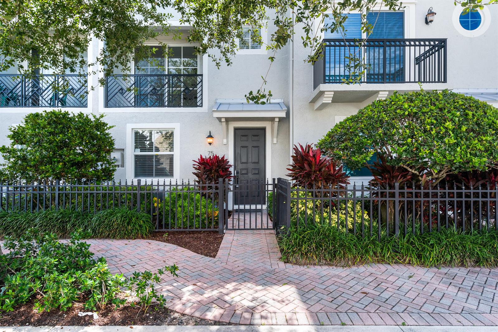 A gray townhouse exterior features a gated brick walkway, a front door, and two balconies — 75 NW 4th Avenue # 75, Delray Beach FL 33444, DELRAY BEACH, FL