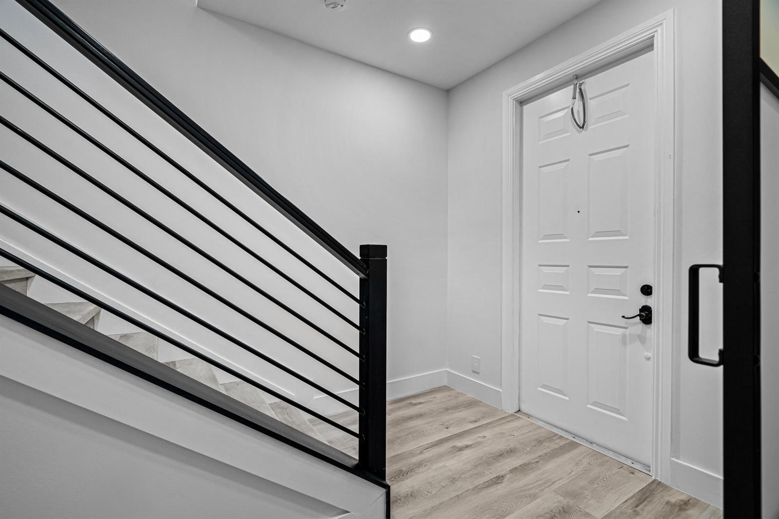 An entryway features light wood-look flooring, a white door, and a staircase with black railings — 75 NW 4th Avenue # 75, Delray Beach FL 33444, DELRAY BEACH, FL