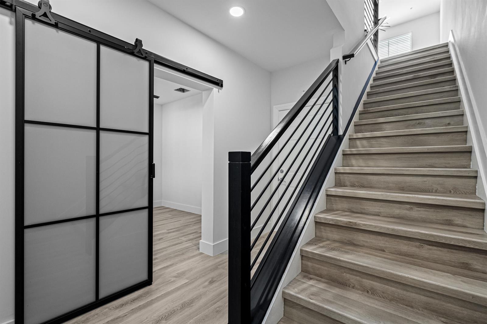 A staircase with black railings sits next to a room with a frosted glass barn door — 75 NW 4th Avenue # 75, Delray Beach FL 33444, DELRAY BEACH, FL