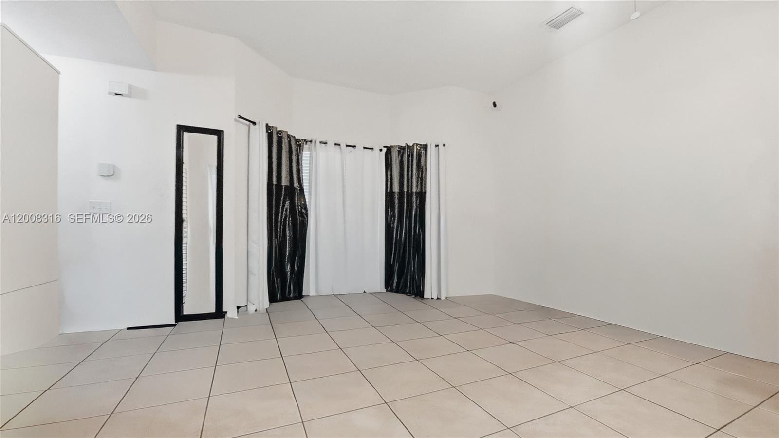 An empty room features white walls, light-colored floor tiles, and a window with curtains — 1978 SE 23rd Ter, Homestead FL 33035, HOMESTEAD, FL