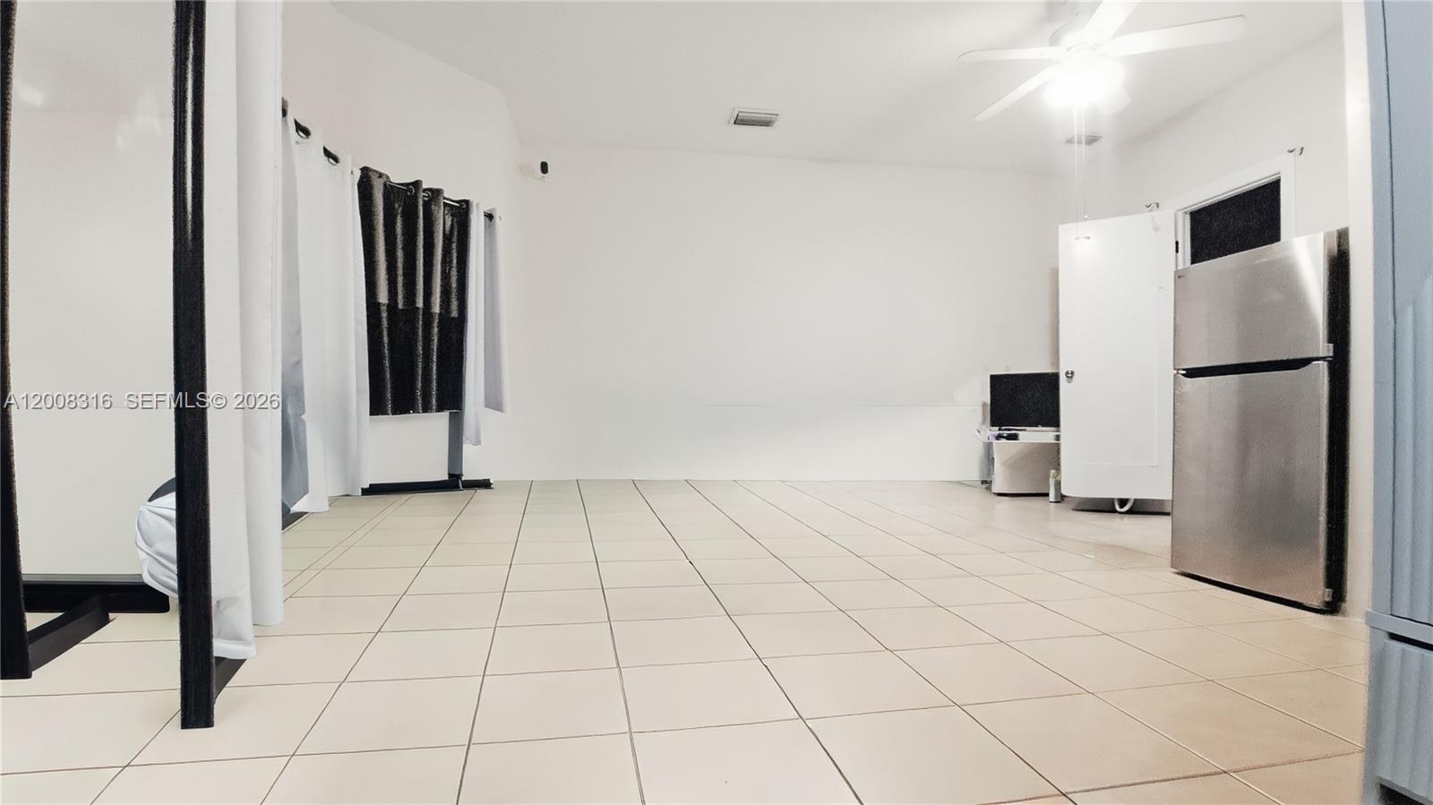 A room with white walls, light-colored tile flooring, a ceiling fan, and a stainless refrigerator — 1978 SE 23rd Ter, Homestead FL 33035, HOMESTEAD, FL