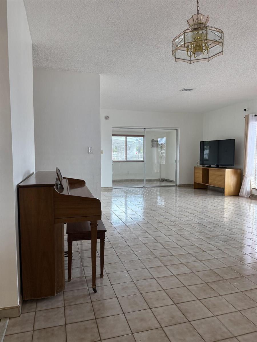 A living room features light tile floors, a wooden piano, and a television on a console — 957 W 67th Street, Hialeah FL 33012, HIALEAH, FL