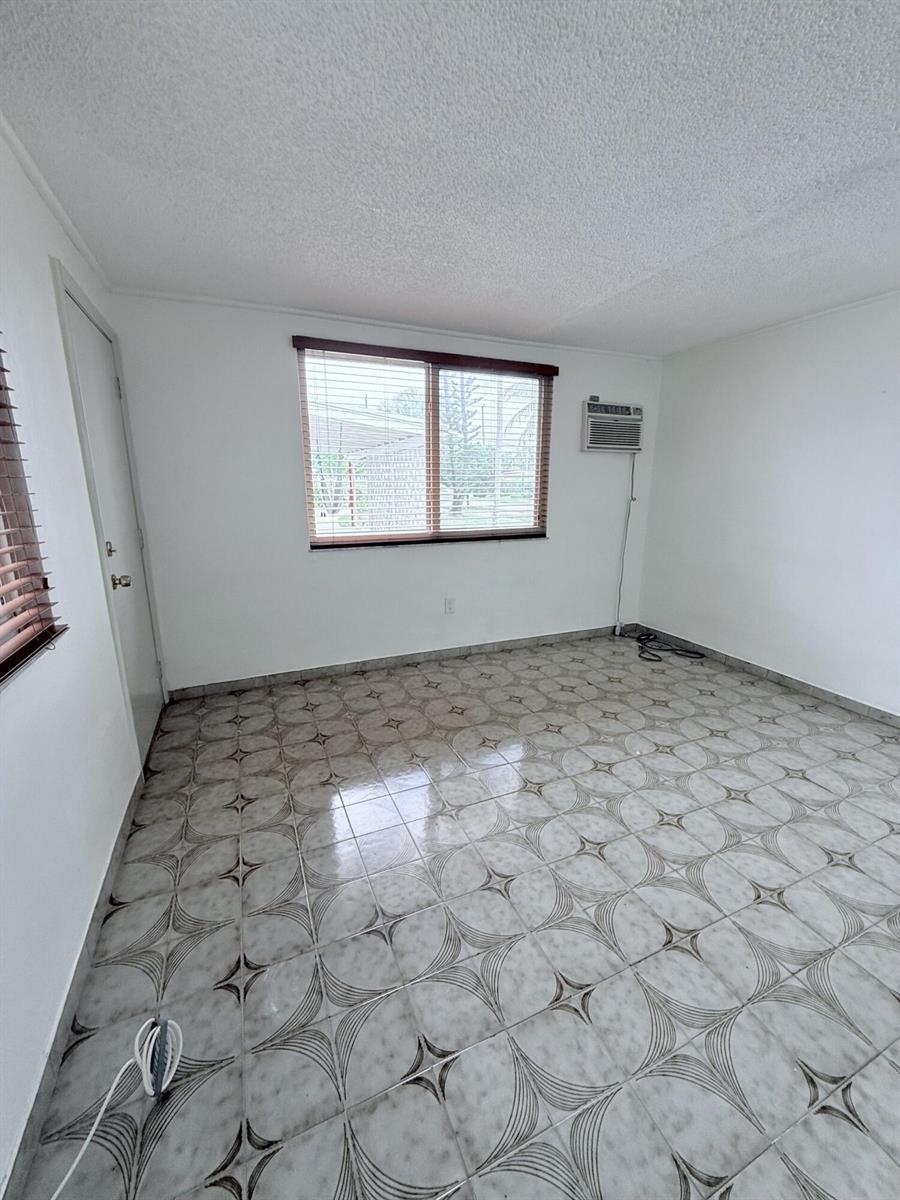 An empty room features white walls, patterned tile flooring, a window with blinds, and an air conditioner — 957 W 67th Street, Hialeah FL 33012, HIALEAH, FL