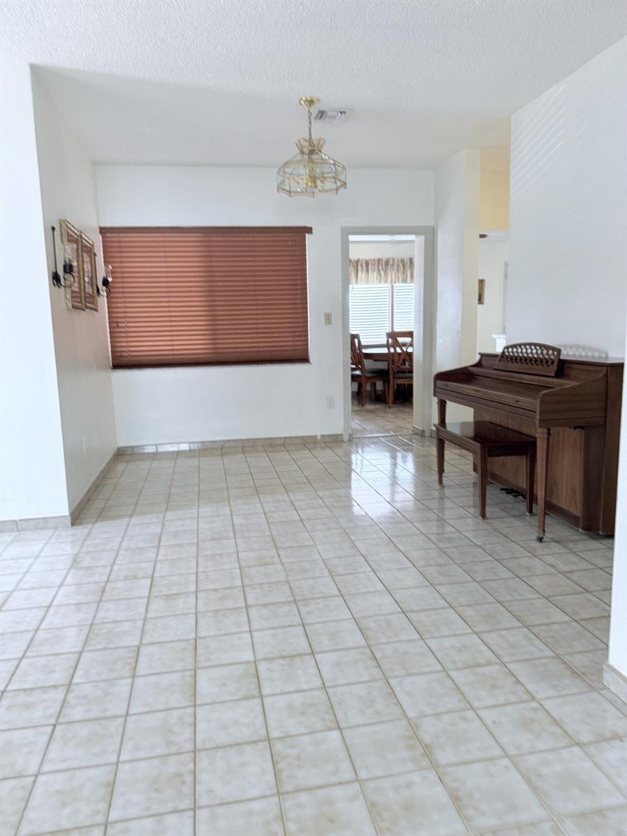 A room with light-colored tile flooring, a piano, and a window with brown blinds — 957 W 67th Street, Hialeah FL 33012, HIALEAH, FL