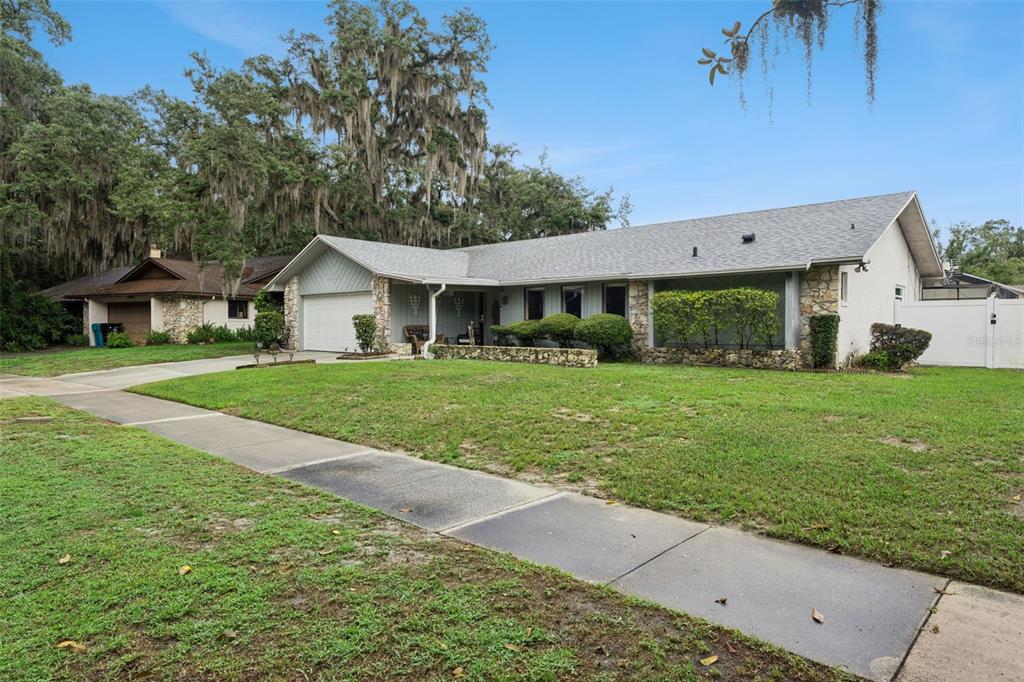 A single-story house with a stone facade, gray roof, and a front lawn with trees — 4902 BRIAR OAKS CIRCLE, ORLANDO, FL
