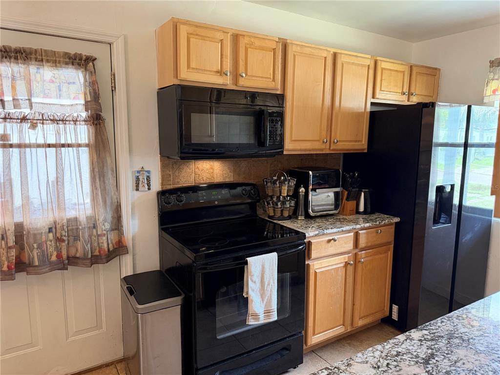 A kitchen features light wood cabinets, black appliances, and granite countertops — 616 DIAL DRIVE, ORLANDO, FL