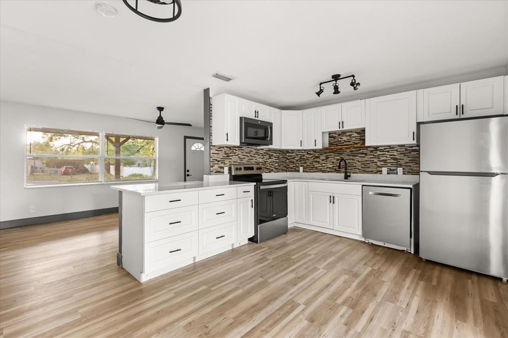 A kitchen features white cabinets, stainless steel appliances, a tiled backsplash, and light wood flooring — 2507 NEWBERRY STREET, ORLANDO, FL