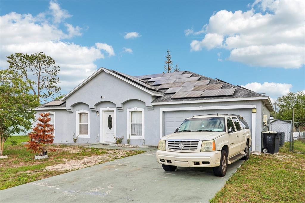 A single-story gray house with solar panels on the roof and a parked SUV — 42 INCONNU DR, POINCIANA, FL