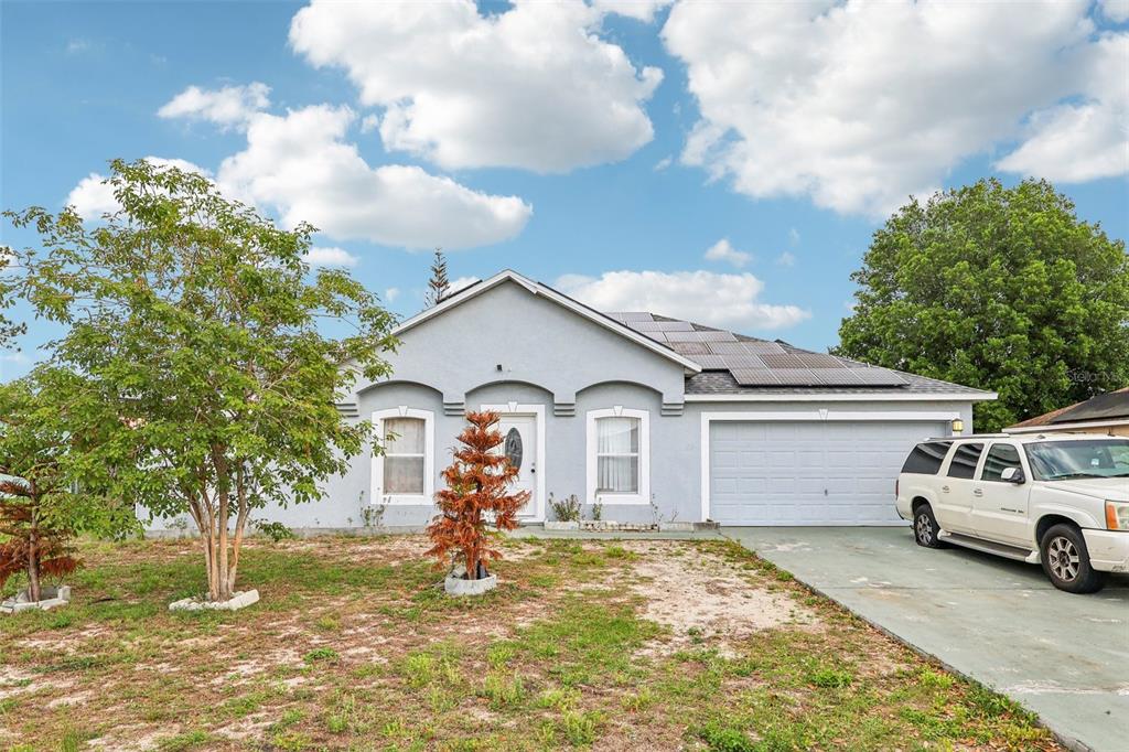 A single-story house with solar panels on the roof, a garage, and a front yard — 42 INCONNU DR, POINCIANA, FL