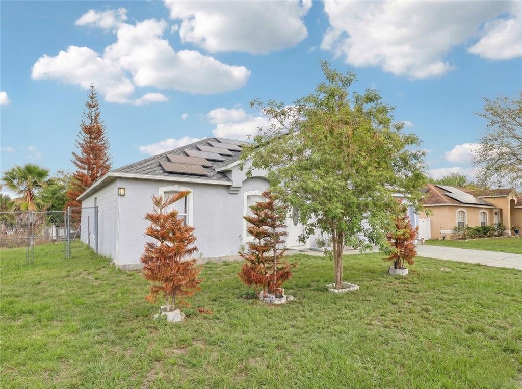 A single-story house with solar panels on the roof and several small trees in front — 42 INCONNU DR, POINCIANA, FL