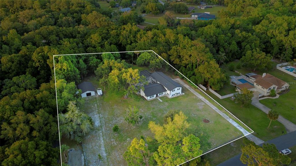 An aerial view shows a house with a detached garage on a large, wooded lot — 155 E COUNTRY CIRCLE DRIVE E, PORT ORANGE, FL