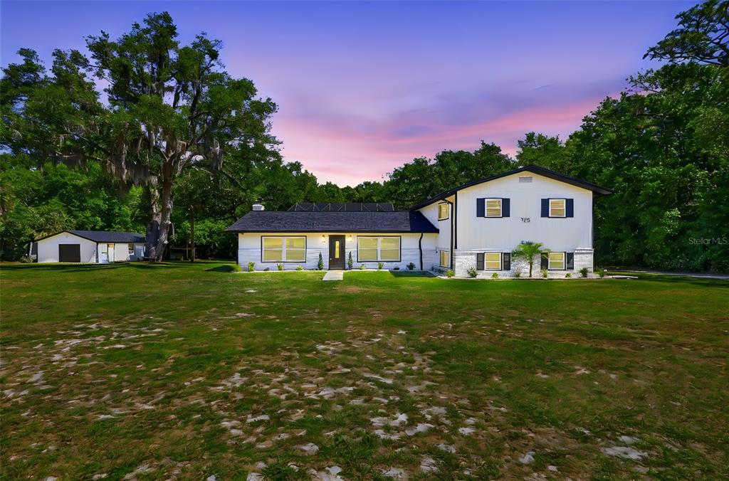 A two-story white house with a dark roof sits on a large, grassy lot — 155 E COUNTRY CIRCLE DRIVE E, PORT ORANGE, FL