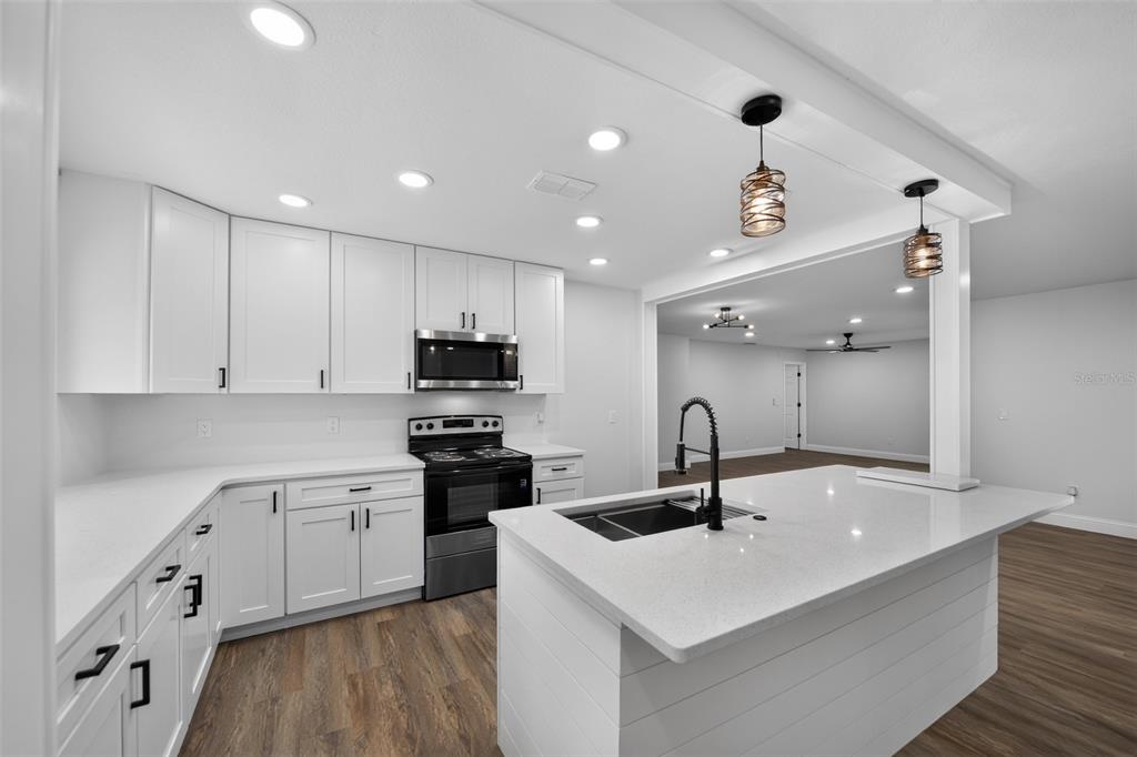 A modern kitchen features white cabinets, a quartz island with a sink, and wood flooring — 12100 CAROLINA WOODS LANE, ORLANDO, FL