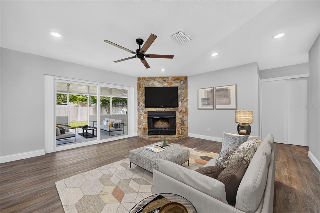 A living room features a stone corner fireplace, sliding glass doors, and wood-look flooring — 12100 CAROLINA WOODS LANE, ORLANDO, FL