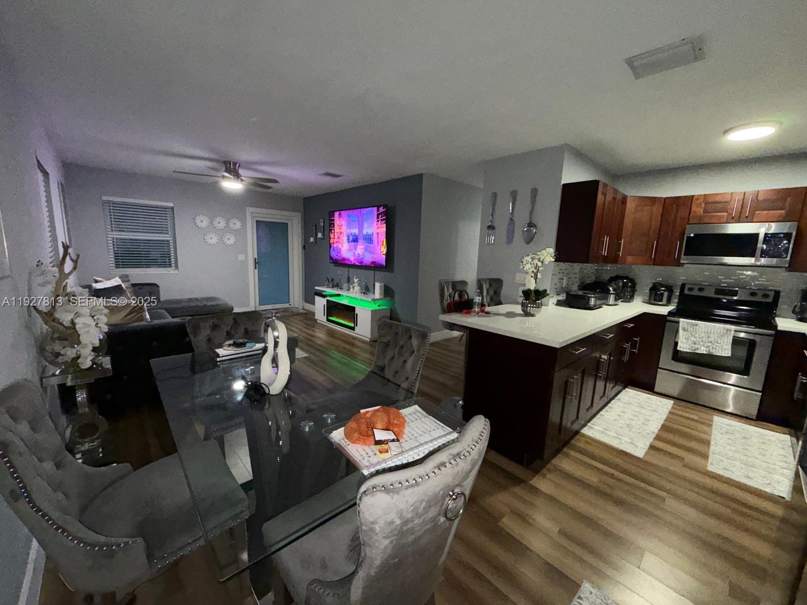 An open-concept living room and kitchen feature dark wood cabinets, stainless appliances, and dining furniture — 100 NE 171st Ter, Miami FL 33162, MIAMI, FL