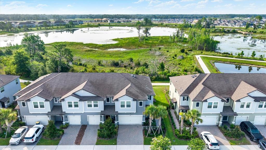 An aerial view shows two multi-unit townhomes with attached garages facing a large pond — 8852 GALLANTREE PLACE, LAND O LAKES, FL