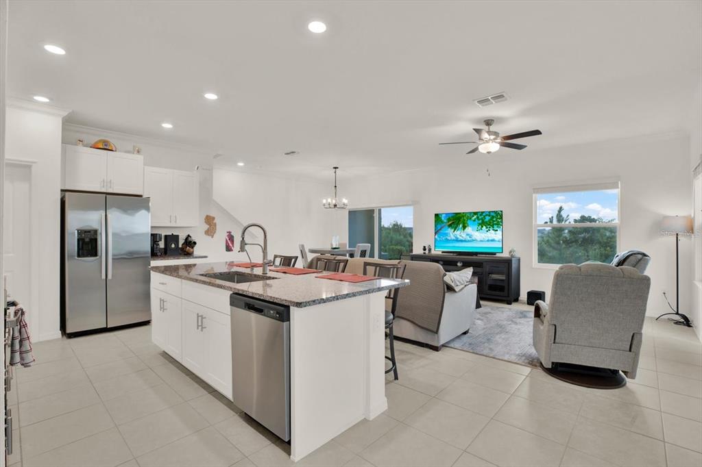 An open-concept kitchen and living area features white cabinetry, a granite island, and tile flooring — 8852 GALLANTREE PLACE, LAND O LAKES, FL