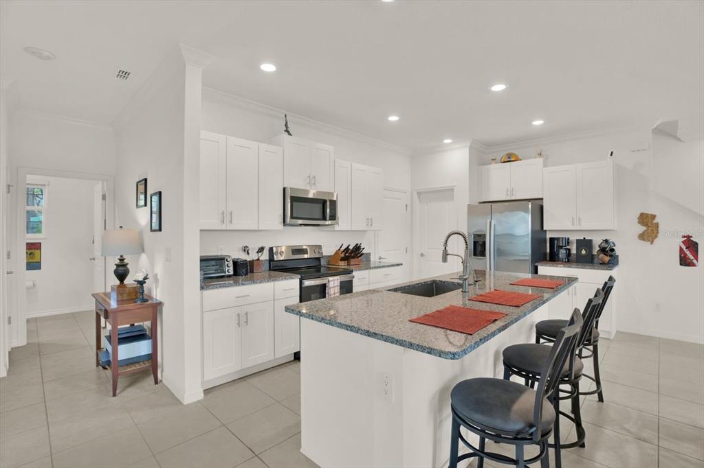 A modern kitchen features white cabinetry, granite countertops, a central island, and stainless steel appliances — 8852 GALLANTREE PLACE, LAND O LAKES, FL