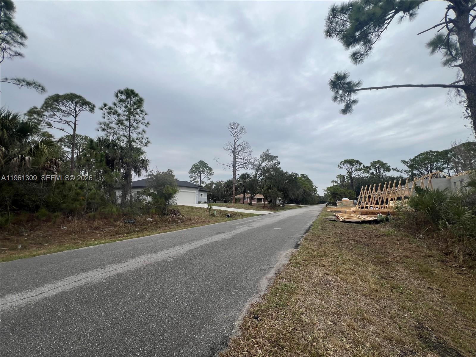 A paved road runs between a residential house and a construction site with wooden trusses — 0 Cloras St, North Port FL 34287, NORTH PORT, FL