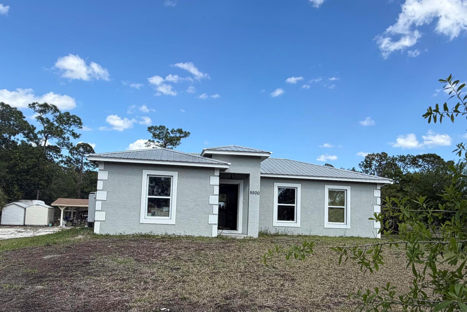 A single-story gray house with a metal roof and white corner accents under a sky — 5500 Hendry Isles Boulevard, Clewiston FL 33440, CLEWISTON, FL