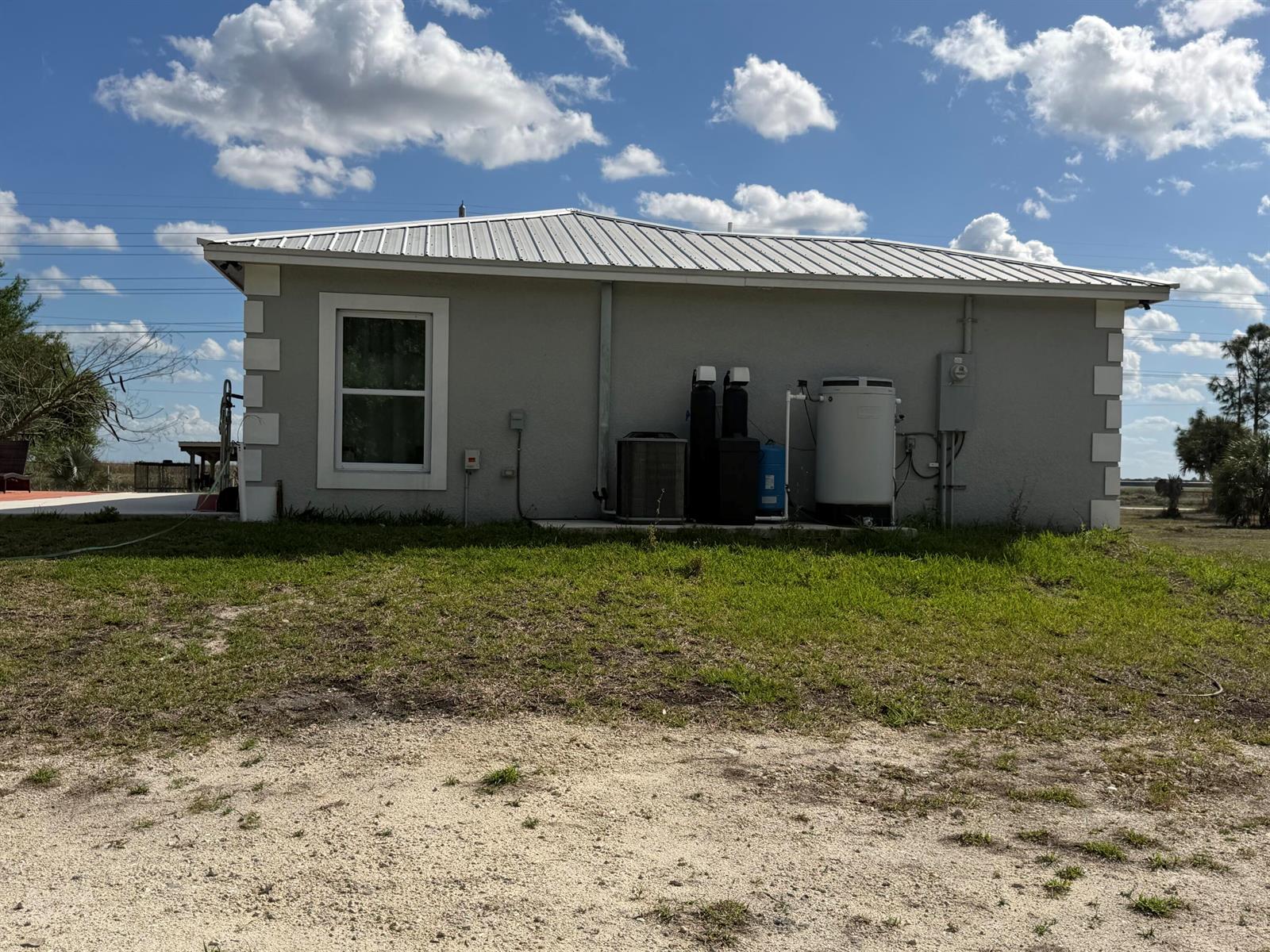 The exterior of a light gray house features a metal roof and water treatment equipment — 5500 Hendry Isles Boulevard, Clewiston FL 33440, CLEWISTON, FL