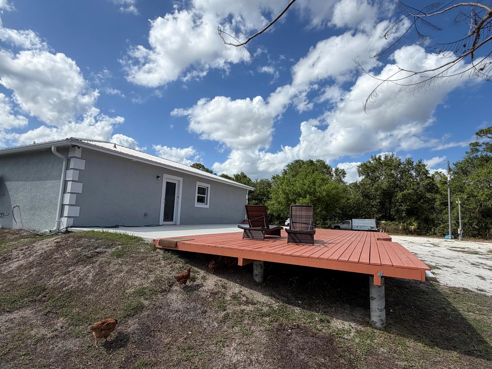 A gray house with a white roof features a raised wooden deck and backyard chickens — 5500 Hendry Isles Boulevard, Clewiston FL 33440, CLEWISTON, FL
