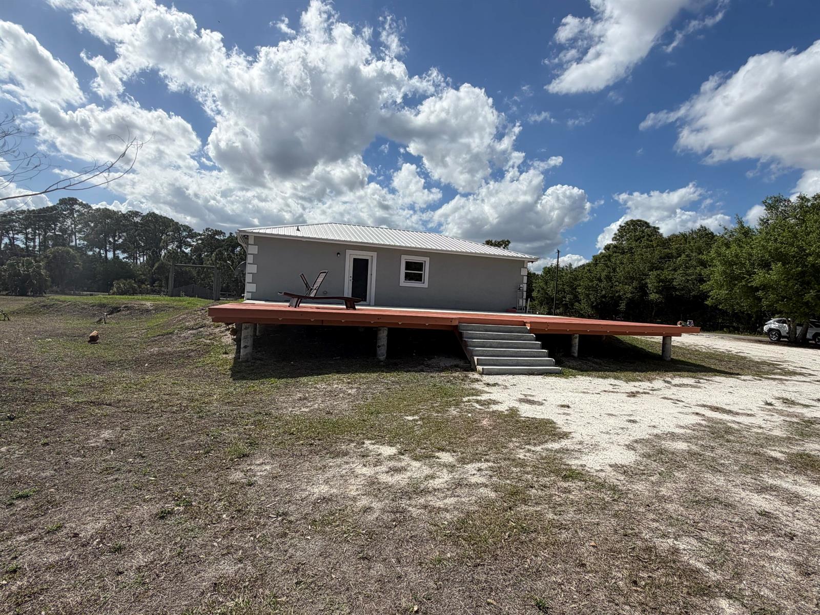 A gray house with a white metal roof features a large wooden deck and stairs — 5500 Hendry Isles Boulevard, Clewiston FL 33440, CLEWISTON, FL