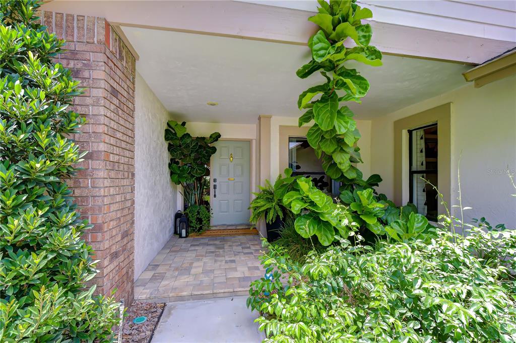 A covered front entryway features a light blue door, brick siding, and lush potted plants — 16126 BELLE MEADE BOULEVARD, ODESSA, FL