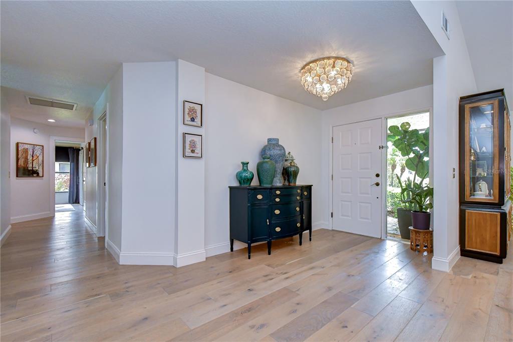 A bright entryway features light wood flooring, a dark chest with vases, and a crystal chandelier — 16126 BELLE MEADE BOULEVARD, ODESSA, FL