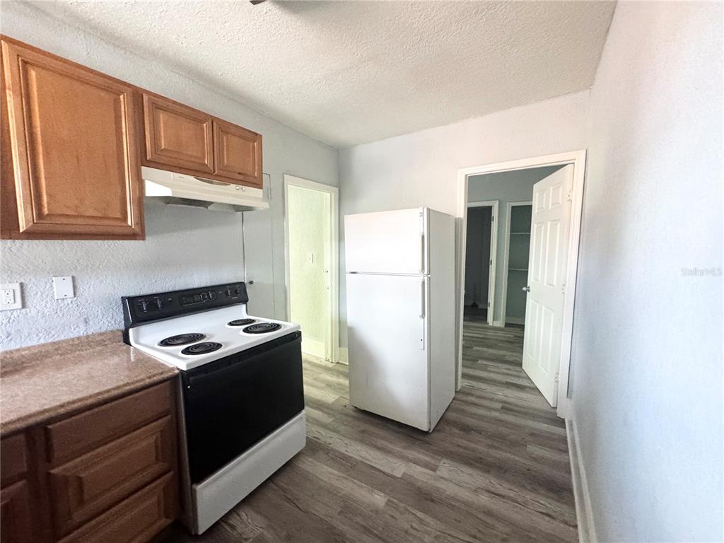 A kitchen features wood cabinets, a black electric stove, a white refrigerator, and wood-look flooring — 704 CORDOVA DRIVE UNIT 6, ORLANDO, FL