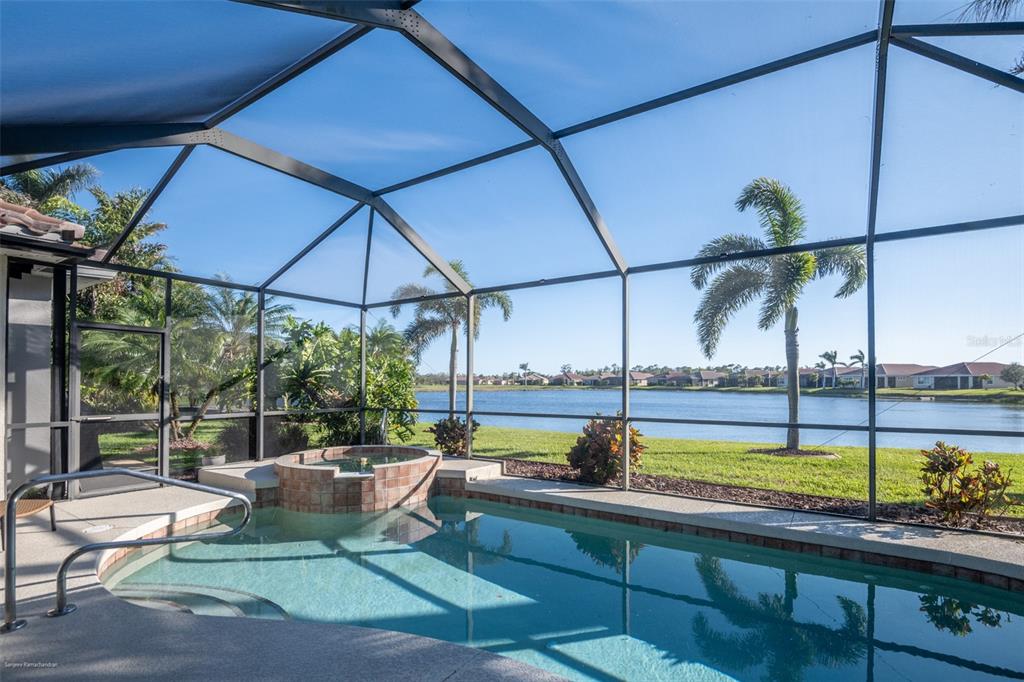 A screened-in pool and spa overlook a lake with palm trees and distant houses — 6571 TALON BAY DRIVE, NORTH PORT, FL