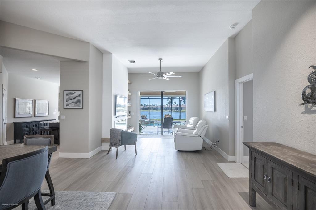 A living room with light wood-look flooring, white walls, a ceiling fan, and sliding glass doors — 6571 TALON BAY DRIVE, NORTH PORT, FL