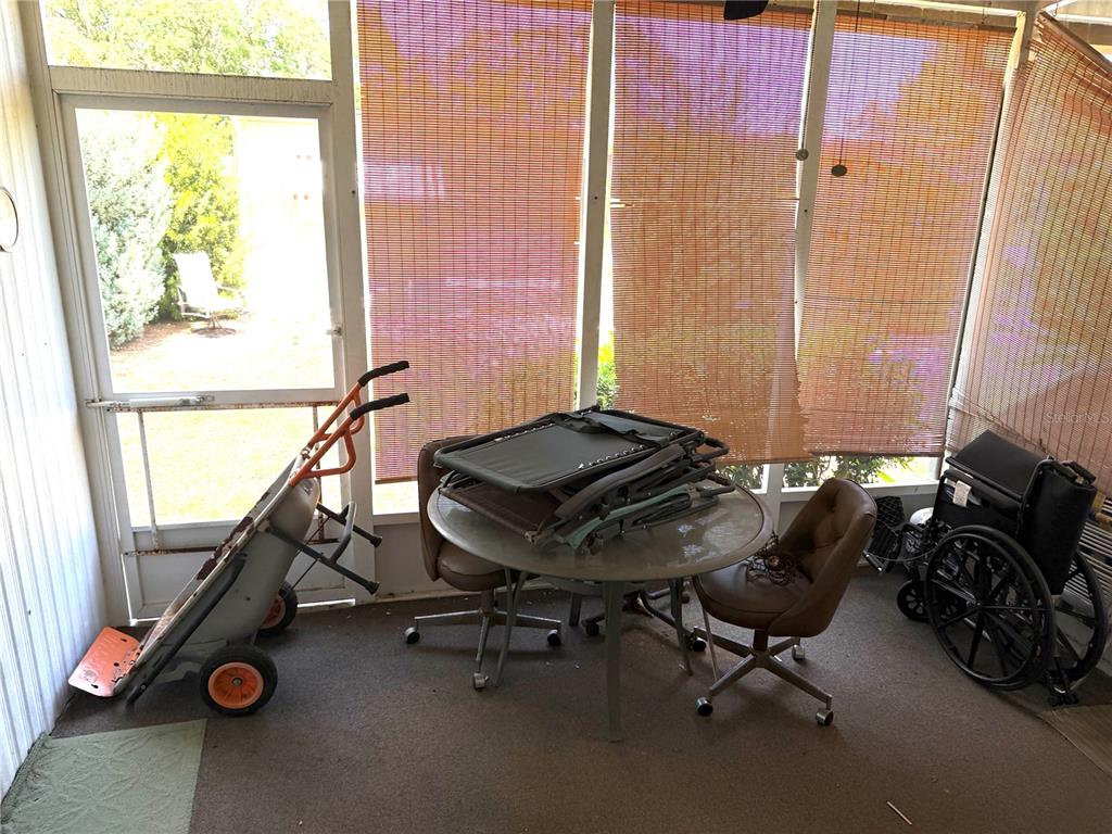 A screened-in porch contains a glass-topped table, chairs, a wheelbarrow, and a wheelchair — 8109 LITTLE TEE LANE, BROOKSVILLE, FL