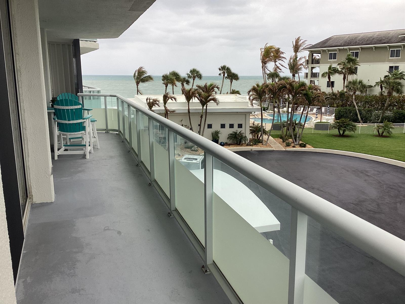 A balcony with a glass railing overlooks a swimming pool, palm trees, and the ocean — 3554 Ocean Drive # 301, Vero Beach FL 32963, VERO BEACH, FL