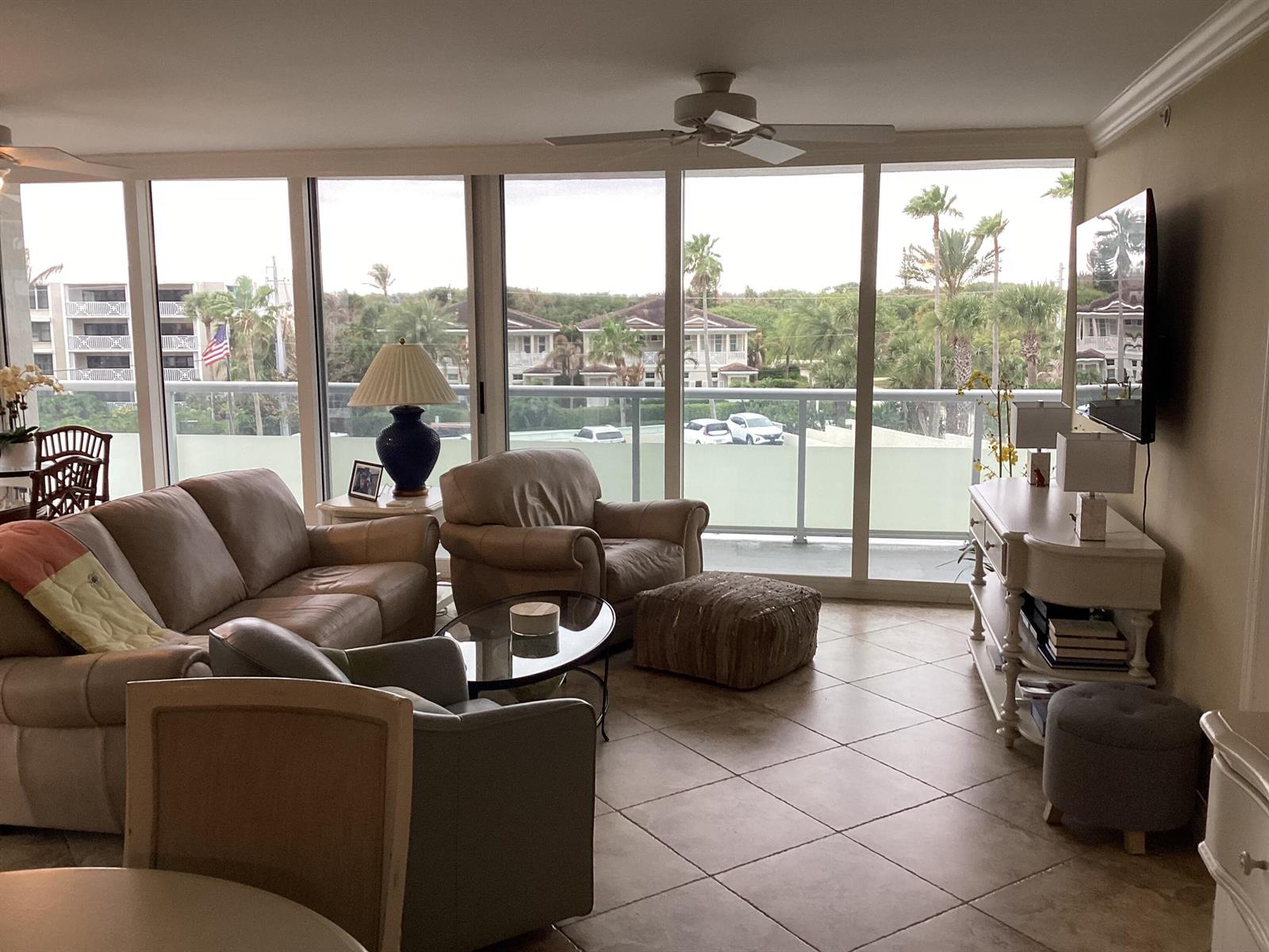 A living room with tile floors, leather furniture, and floor-to-ceiling windows overlooking a tropical landscape — 3554 Ocean Drive # 301, Vero Beach FL 32963, VERO BEACH, FL