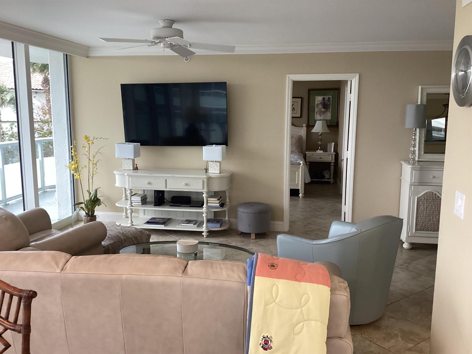 A living room with a wall-mounted television, white console, beige sofa, and an adjacent bedroom — 3554 Ocean Drive # 301, Vero Beach FL 32963, VERO BEACH, FL