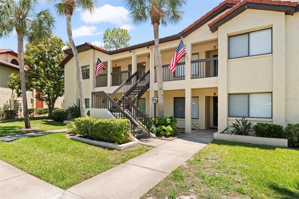 A two-story apartment building with tan stucco walls, a brown roof, and exterior staircases — 1801 E LAKE ROAD UNIT 4E, PALM HARBOR, FL