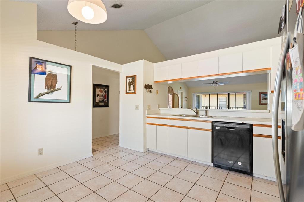 A kitchen with white cabinets, a black dishwasher, and tile flooring opens to a sunroom — 1801 E LAKE ROAD UNIT 4E, PALM HARBOR, FL