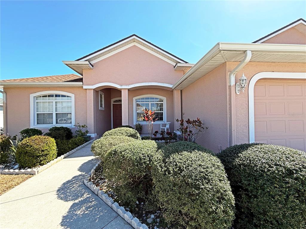A pink stucco house exterior features a concrete walkway, rounded shrubs, and a garage — 9011 PROVINCE STREET, SARASOTA, FL