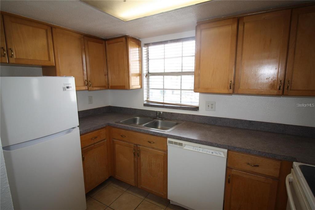 A kitchen features wood cabinets, a white refrigerator, a dishwasher, and a double-basin sink — 1000 S SEMORAN BOULEVARD UNIT 306, WINTER PARK, FL