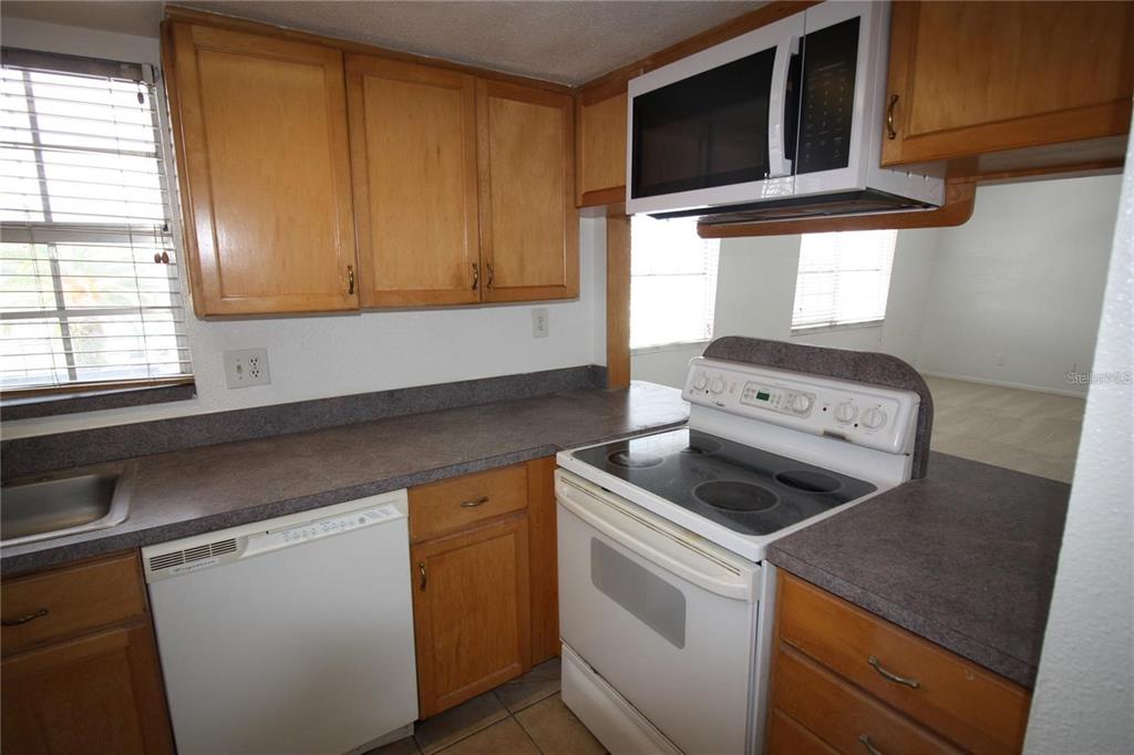 A kitchen features wood cabinets, white appliances, and gray laminate countertops — 1000 S SEMORAN BOULEVARD UNIT 306, WINTER PARK, FL