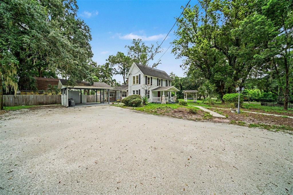 A two-story white house with a covered carport sits on a large gravel lot — 1509 W WINDHORST ROAD, BRANDON, FL