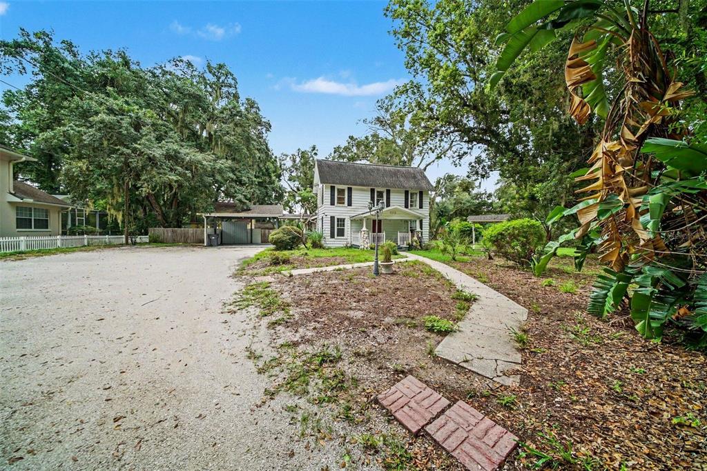 A two-story white house with a front porch sits behind a gravel driveway and trees — 1509 W WINDHORST ROAD, BRANDON, FL