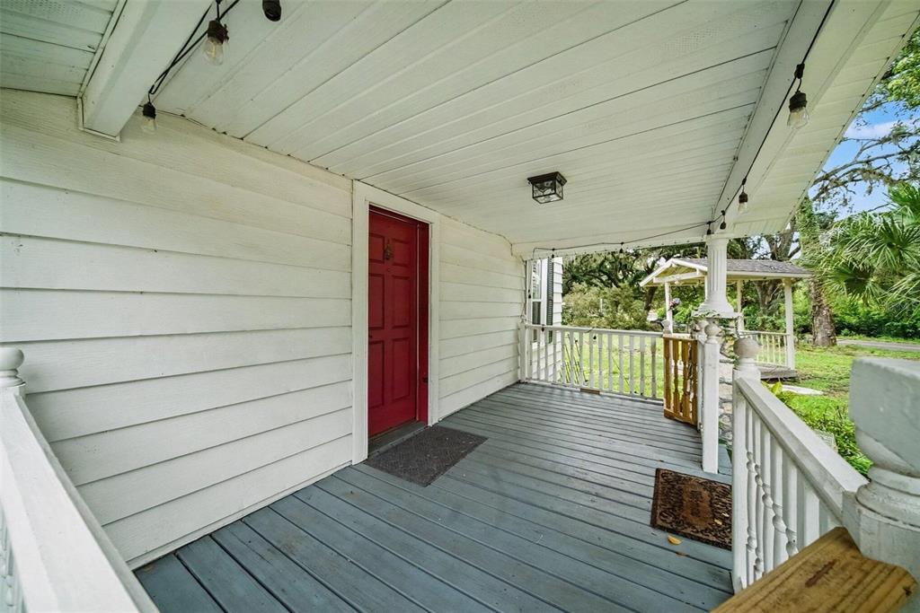 A covered front porch features white horizontal siding, a red door, and grey wooden decking — 1509 W WINDHORST ROAD, BRANDON, FL