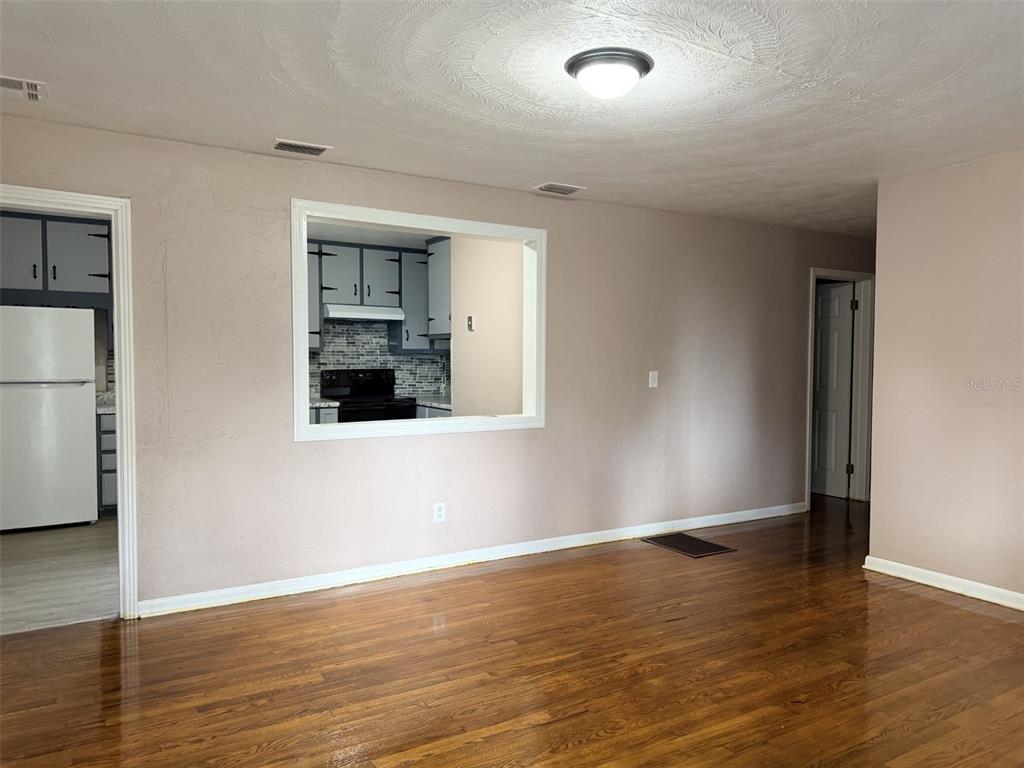 A living room with hardwood floors, a ceiling light, and a pass-through window to the kitchen — 1025 NE 4TH STREET, CHIEFLAND, FL
